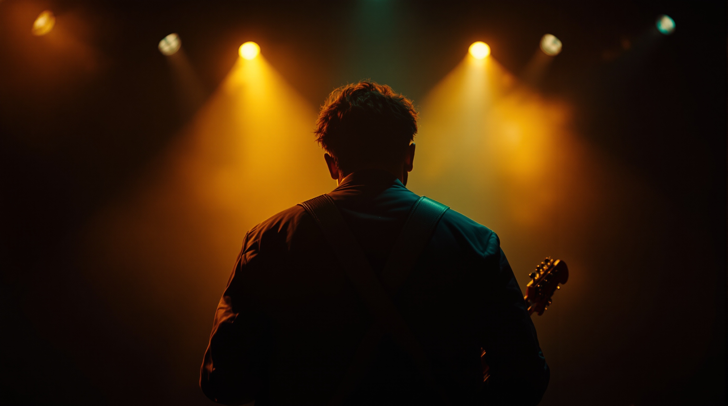 Muzyk z gitarą w ciepłym świetle sceny, od tyłu